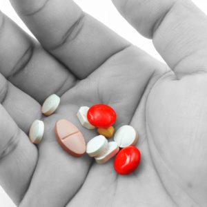 Black and white photo of a person's hand holding pills that are in color.