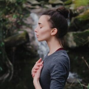 Picture of a woman deep breathing by a waterfall.