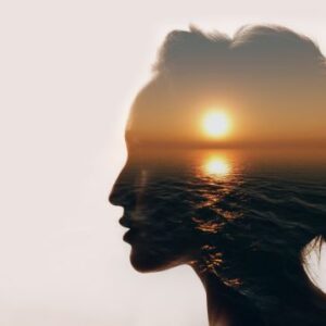 Side profile silhouette of a woman's face, with the ocean and a sunset filling the silhouette