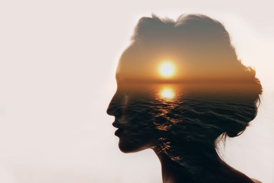 Side profile silhouette of a woman's face, with the ocean and a sunset filling the silhouette